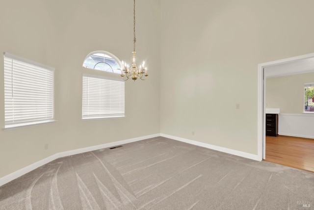 carpeted spare room with baseboards, a high ceiling, visible vents, and a notable chandelier