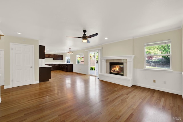 unfurnished living room featuring ceiling fan, a wealth of natural light, wood finished floors, and a tile fireplace