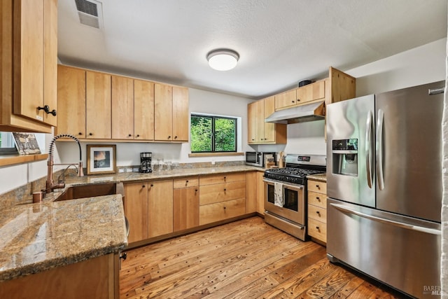 kitchen featuring visible vents, light brown cabinets, under cabinet range hood, a sink, and appliances with stainless steel finishes