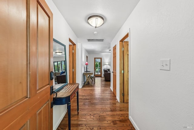 hallway with visible vents, baseboards, and dark wood-type flooring
