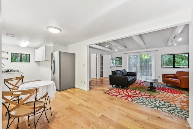 living area featuring baseboards, beam ceiling, light wood-style flooring, and rail lighting