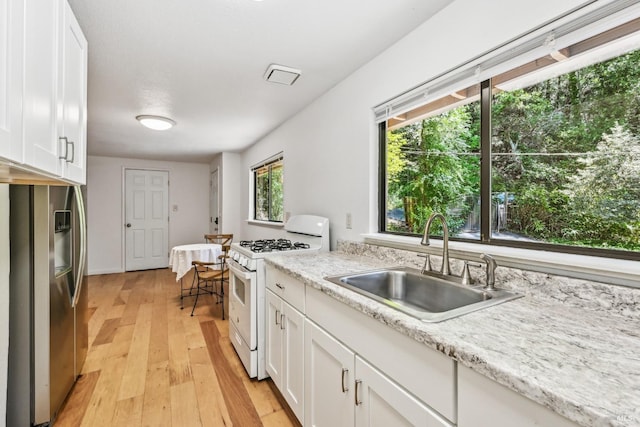 kitchen featuring light wood-style floors, a sink, white range with gas cooktop, and white cabinetry