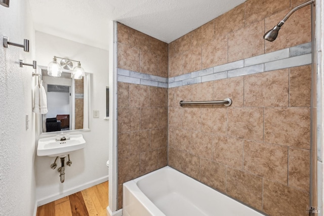 bathroom with a textured ceiling, wood finished floors, baseboards, toilet, and shower / bathtub combination