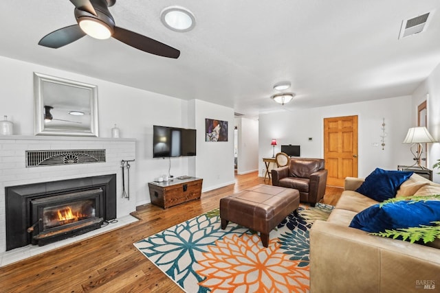 living area with a brick fireplace, ceiling fan, visible vents, and hardwood / wood-style flooring