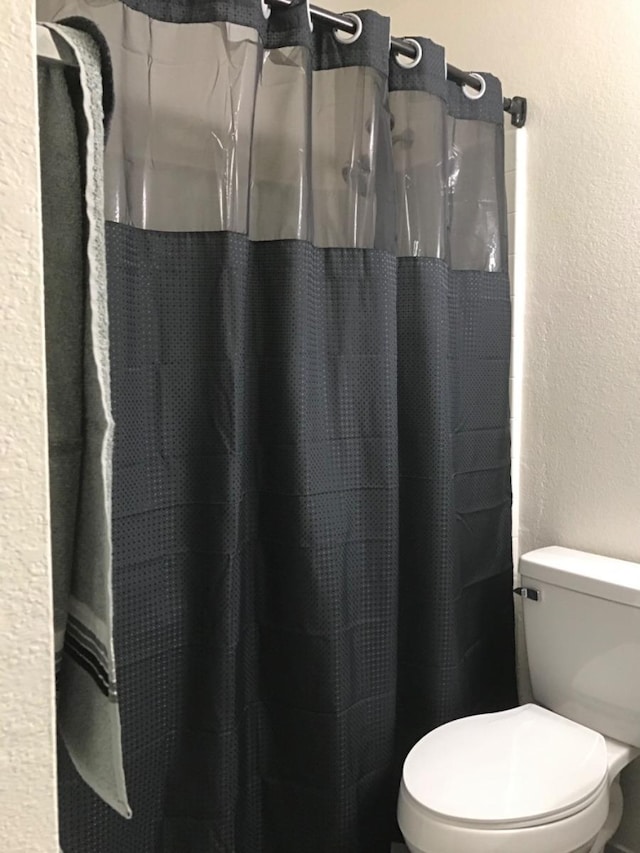 bathroom featuring toilet, a textured wall, and a shower with shower curtain