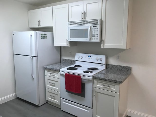 kitchen with white appliances, dark wood finished floors, dark stone counters, white cabinetry, and baseboards