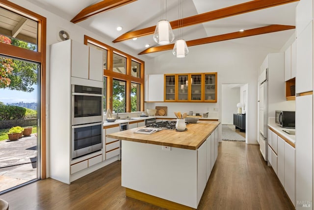 kitchen featuring dark wood-style flooring, beamed ceiling, butcher block countertops, white cabinetry, and stainless steel appliances
