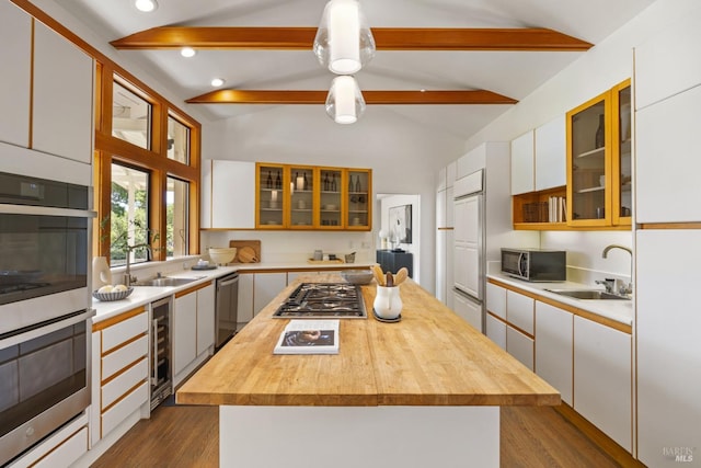 kitchen with a sink, lofted ceiling with beams, butcher block countertops, appliances with stainless steel finishes, and wine cooler