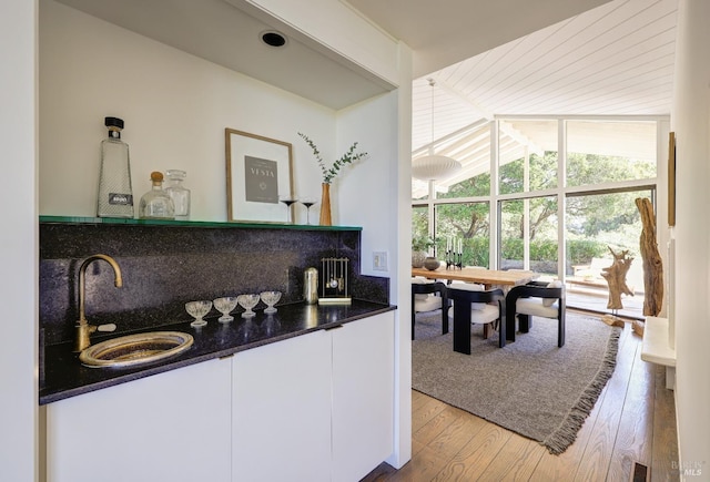bar featuring light wood finished floors, indoor wet bar, a sink, decorative backsplash, and lofted ceiling