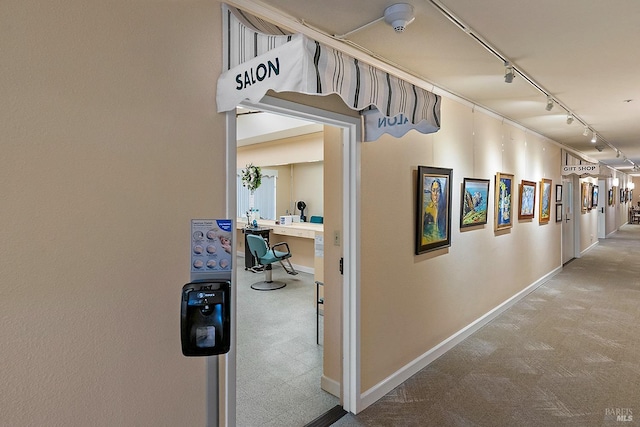 corridor featuring rail lighting, baseboards, and carpet