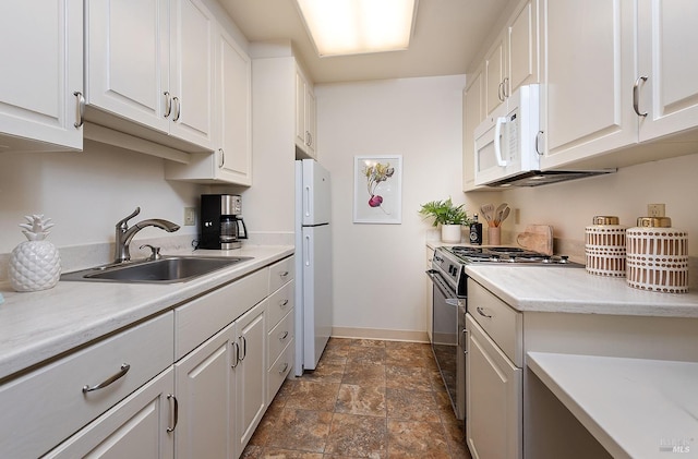 kitchen with white cabinets, a sink, white appliances, stone finish floor, and baseboards