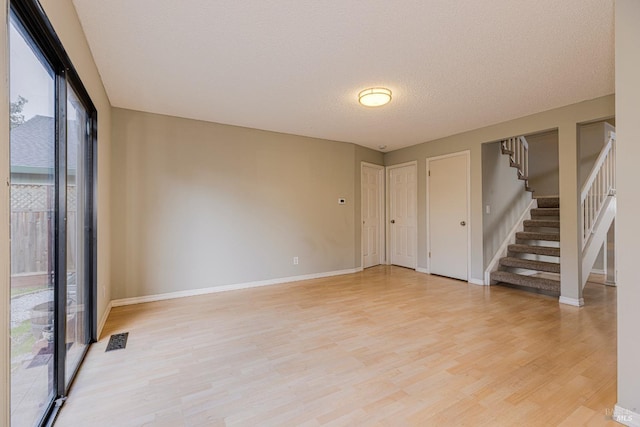 empty room with a textured ceiling, visible vents, light wood-type flooring, baseboards, and stairs
