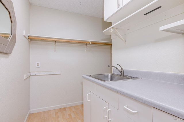 laundry area with a sink, baseboards, a textured ceiling, and light wood-style flooring
