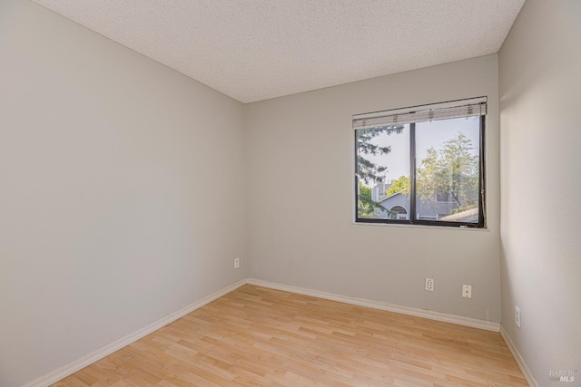 spare room with baseboards, a textured ceiling, and light wood-style flooring