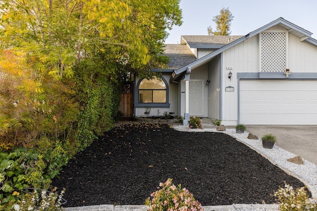 view of exterior entry with an attached garage, roof with shingles, and concrete driveway