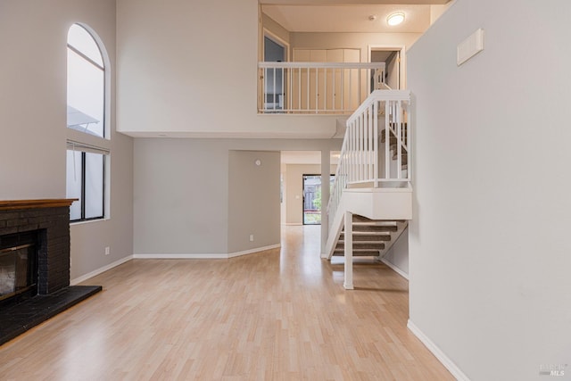 unfurnished living room with stairs, a towering ceiling, wood finished floors, a fireplace, and baseboards