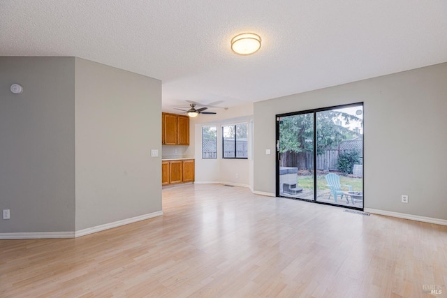 unfurnished living room featuring light wood-style floors, a textured ceiling, a ceiling fan, baseboards, and visible vents
