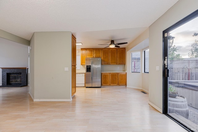 kitchen with ceiling fan, light wood finished floors, dishwasher, a brick fireplace, and stainless steel refrigerator with ice dispenser