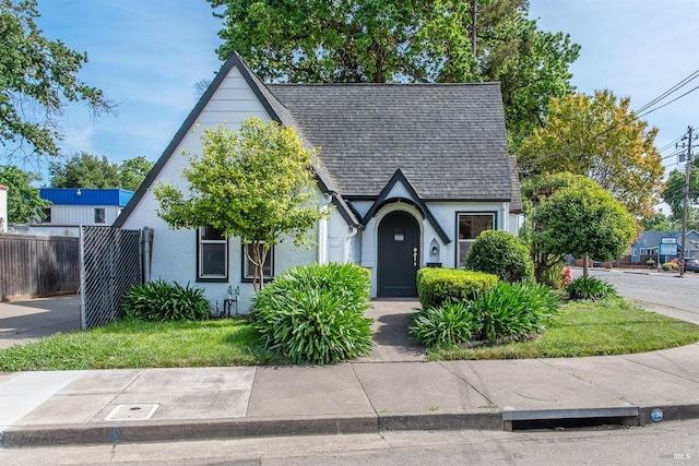english style home featuring fence, stucco siding, and roof with shingles