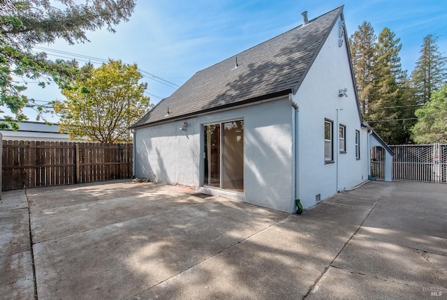 rear view of house featuring roof with shingles, fence, a patio, and stucco siding