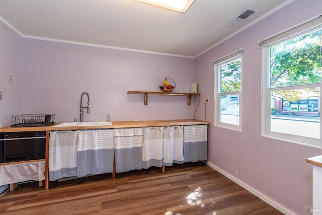interior space featuring a sink, baseboards, wood finished floors, visible vents, and ornamental molding