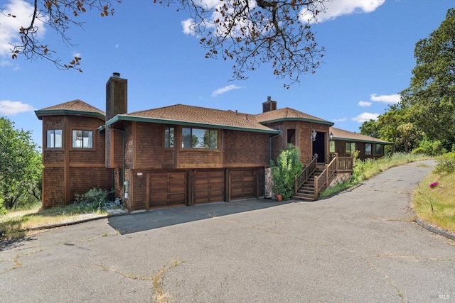 view of front of property featuring a garage, a chimney, and driveway