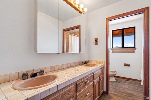 bathroom with toilet, double vanity, a sink, and wood finished floors