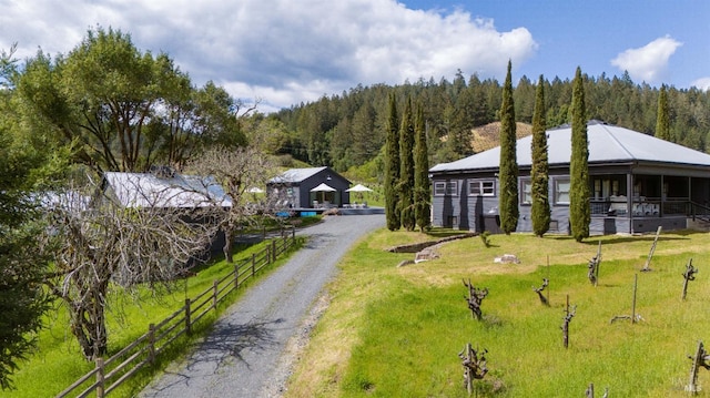 exterior space featuring a forest view, driveway, fence, and a front lawn