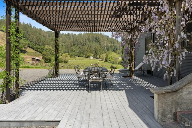 wooden terrace featuring a pergola, a wooded view, and outdoor dining space