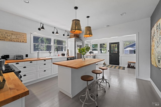 kitchen with wood finished floors, butcher block countertops, a breakfast bar area, white cabinets, and a sink