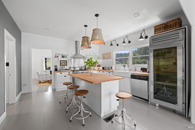 kitchen with white cabinets, appliances with stainless steel finishes, wood counters, wall chimney exhaust hood, and a kitchen bar
