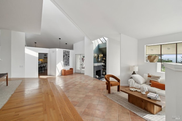 living room with high vaulted ceiling, a tiled fireplace, and light wood-style floors