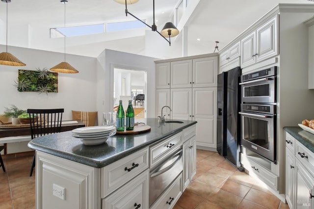 kitchen with dark countertops, a center island with sink, a sink, a warming drawer, and black fridge