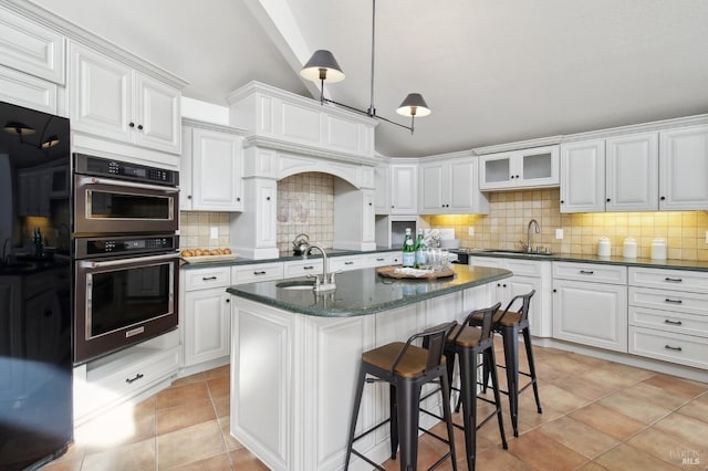 kitchen with a sink, light tile patterned floors, white cabinets, and backsplash