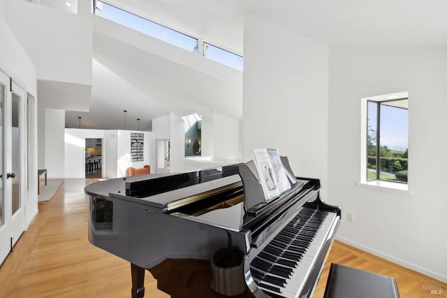 living area featuring plenty of natural light, light wood-style floors, baseboards, and high vaulted ceiling