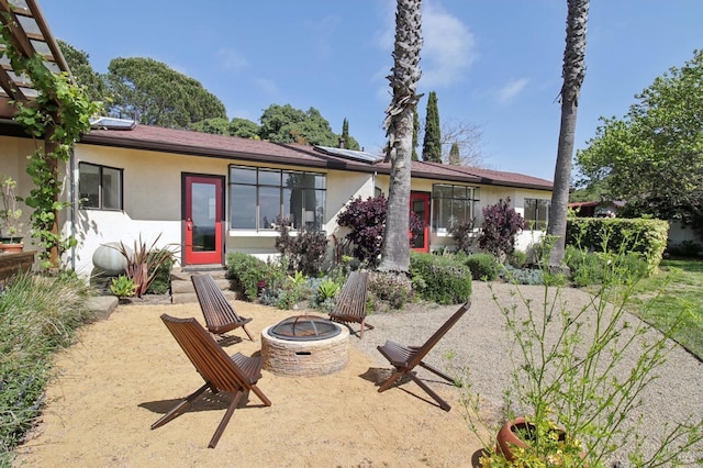 rear view of house with a fire pit, solar panels, and stucco siding