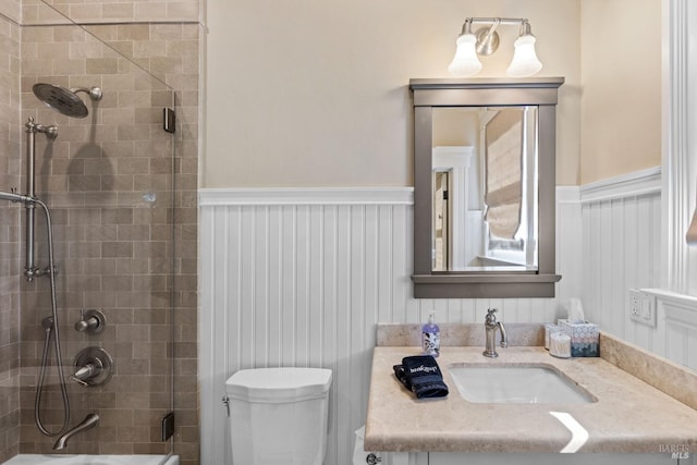bathroom with vanity, toilet, a shower with door, and a wainscoted wall