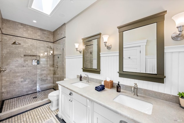 full bath featuring toilet, a tile shower, a sink, and a wainscoted wall