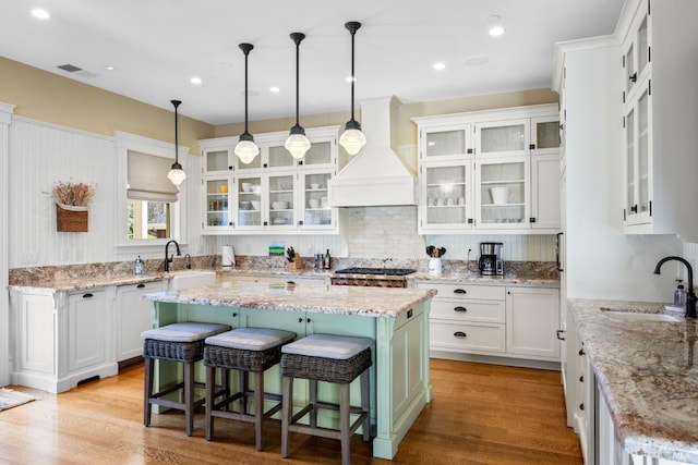 kitchen with visible vents, premium range hood, a center island, white cabinetry, and a sink