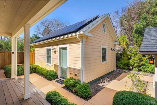 exterior space with roof mounted solar panels and fence