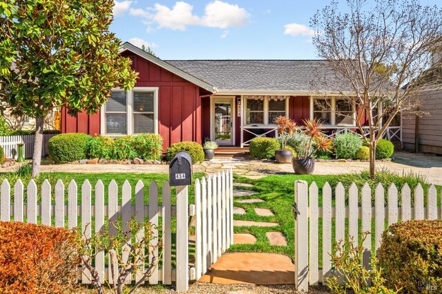 view of front of house featuring roof with shingles, board and batten siding, a fenced front yard, and a front yard