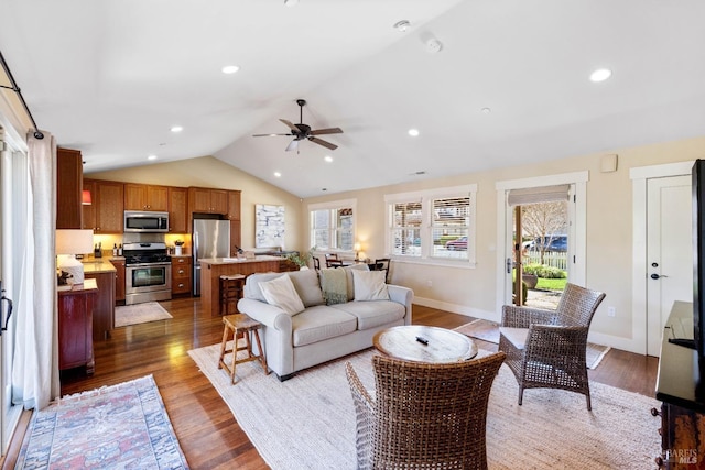 living area featuring a ceiling fan, wood finished floors, a healthy amount of sunlight, and vaulted ceiling