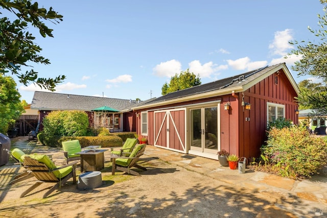 rear view of house featuring french doors, board and batten siding, a fire pit, and a patio area