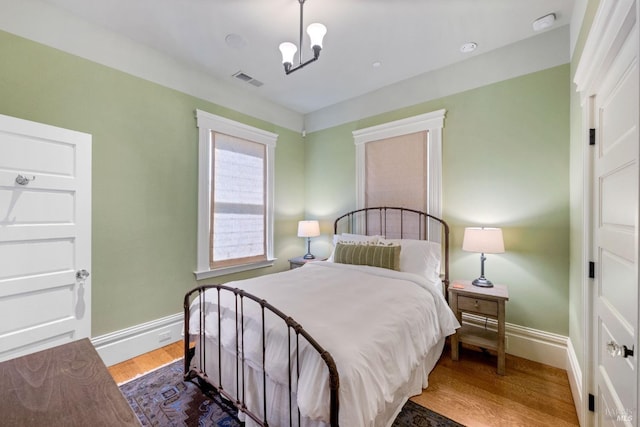 bedroom featuring visible vents, baseboards, wood finished floors, and a notable chandelier