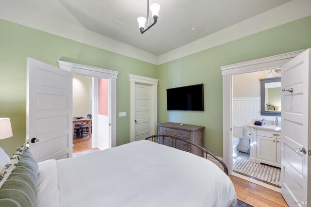 bedroom with a sink, light wood-style floors, a chandelier, ensuite bathroom, and a closet