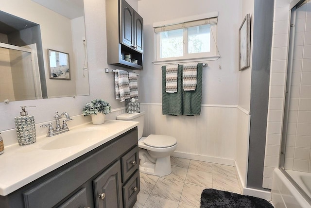 bathroom featuring wainscoting, vanity, toilet, marble finish floor, and bath / shower combo with glass door