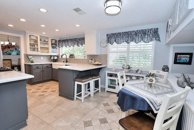 kitchen with a kitchen breakfast bar, backsplash, visible vents, a sink, and glass insert cabinets