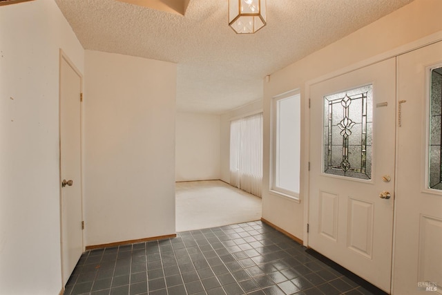 entryway with a textured ceiling, dark tile patterned flooring, and baseboards