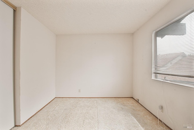 spare room featuring light carpet and a textured ceiling