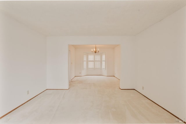 empty room with a chandelier, light colored carpet, and baseboards